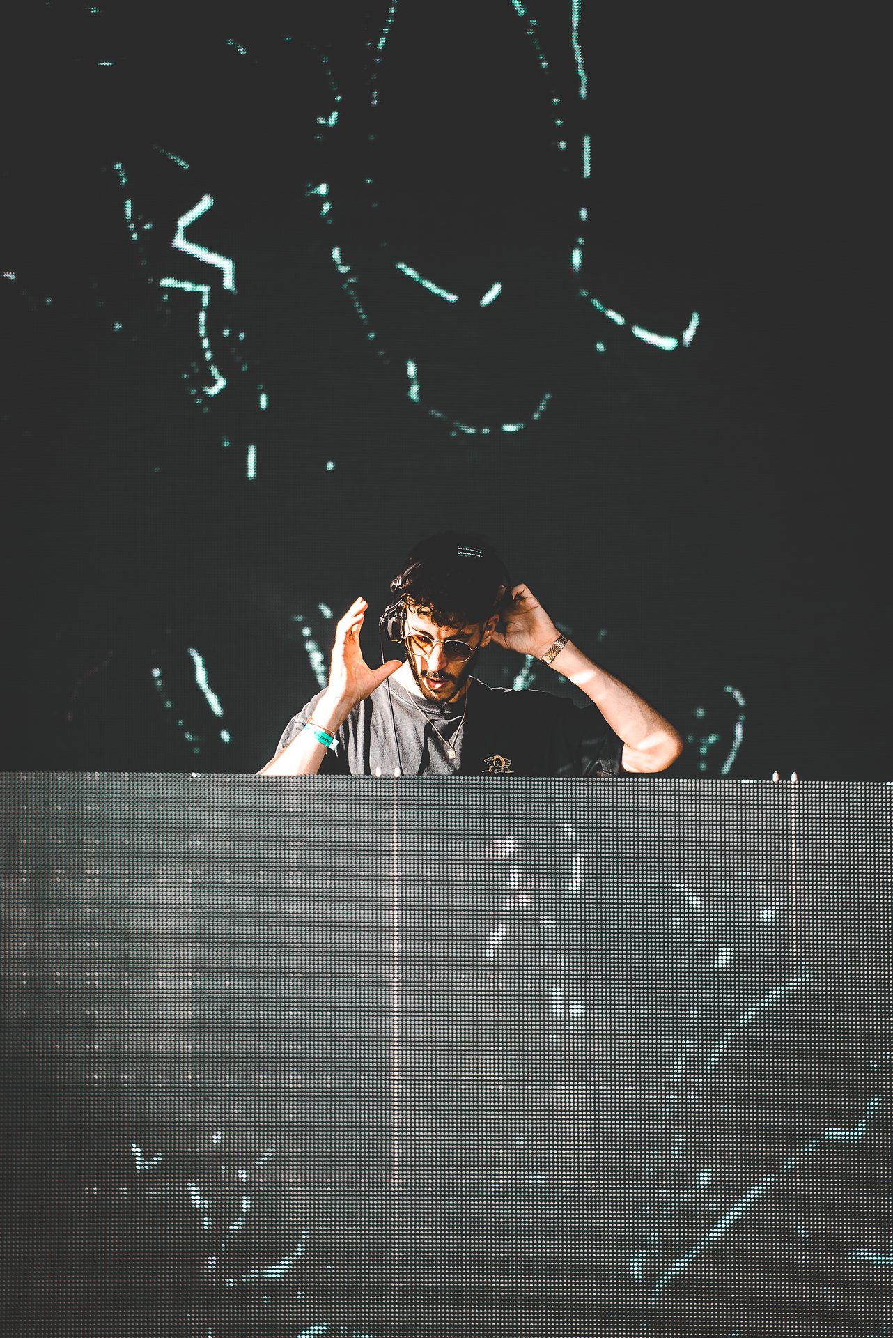 NOFONE performing live on stage at a club, hands raised behind the DJ booth